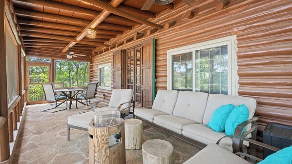 A log cabin with a stone patio, a sofa with pillows, and a dining table with chairs.