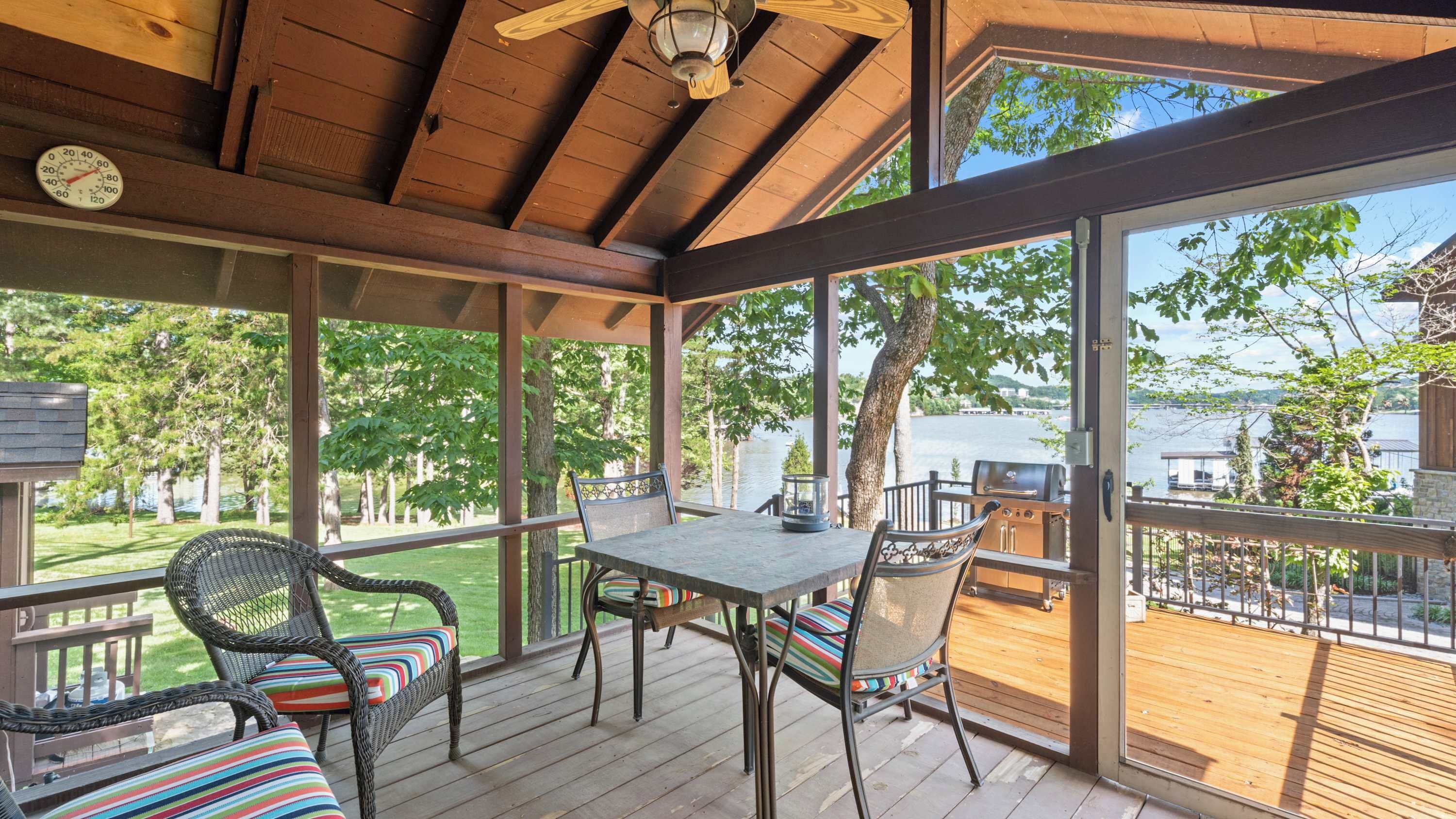 A covered outdoor deck with a table and chairs, overlooking a body of water.