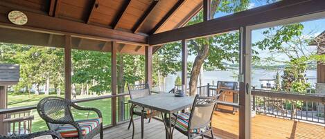 A covered outdoor deck with a table and chairs, overlooking a body of water.