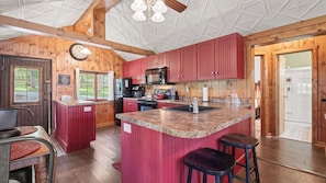 A kitchen with wooden walls, a central island, and red cabinets.