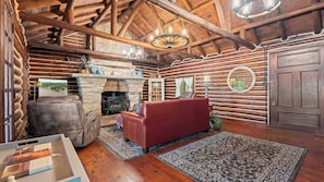A log cabin interior with a stone fireplace, leather sofa, and a wooden ceiling.