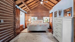 A log cabin interior with a bed, dresser, and a ceiling fan.