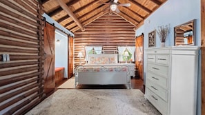 A log cabin interior with a bed, dresser, and a ceiling fan.