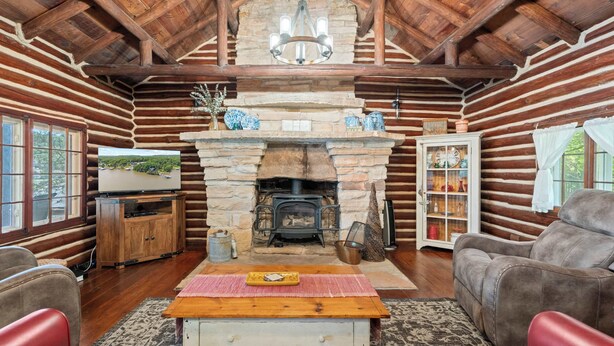 A log cabin interior with a stone fireplace, wooden furniture, and a television on a wooden stand.