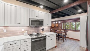 A kitchen with white cabinets, a microwave, an oven, and a dining area with a table and chairs.