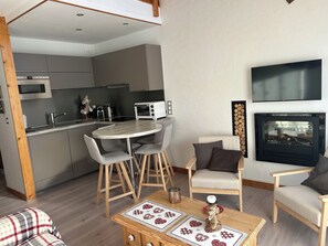 Eine moderne Küche mit Mikrowelle, Toaster und Spüle. Ein Esstisch mit Stühlen und ein Kamin, über dem sich ein Fernseher befindet.