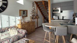 A modern kitchen with a built-in oven and microwave, a wooden staircase, and a dining area with bar stools. - Cosy duplex in the Haut-Jura with detached garage. (PREMANON)