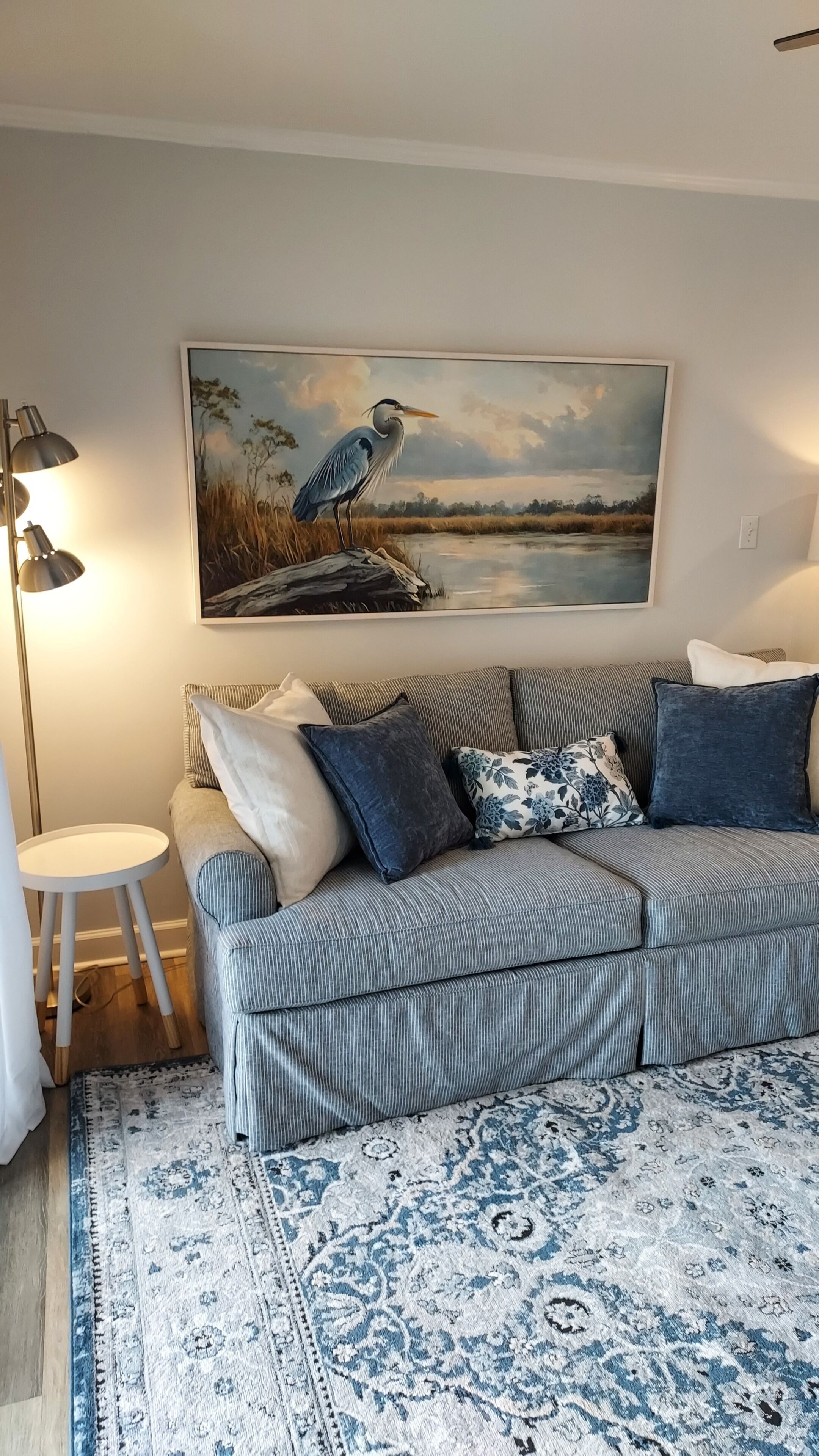 Una sala de estar con un sofá a rayas, un tapete estampado, un cuadro de un pájaro y una lámpara.