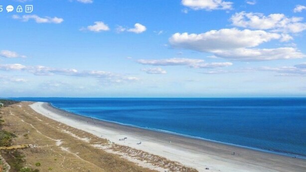 Une plage côtière, avec un ciel dégagé et quelques nuages.