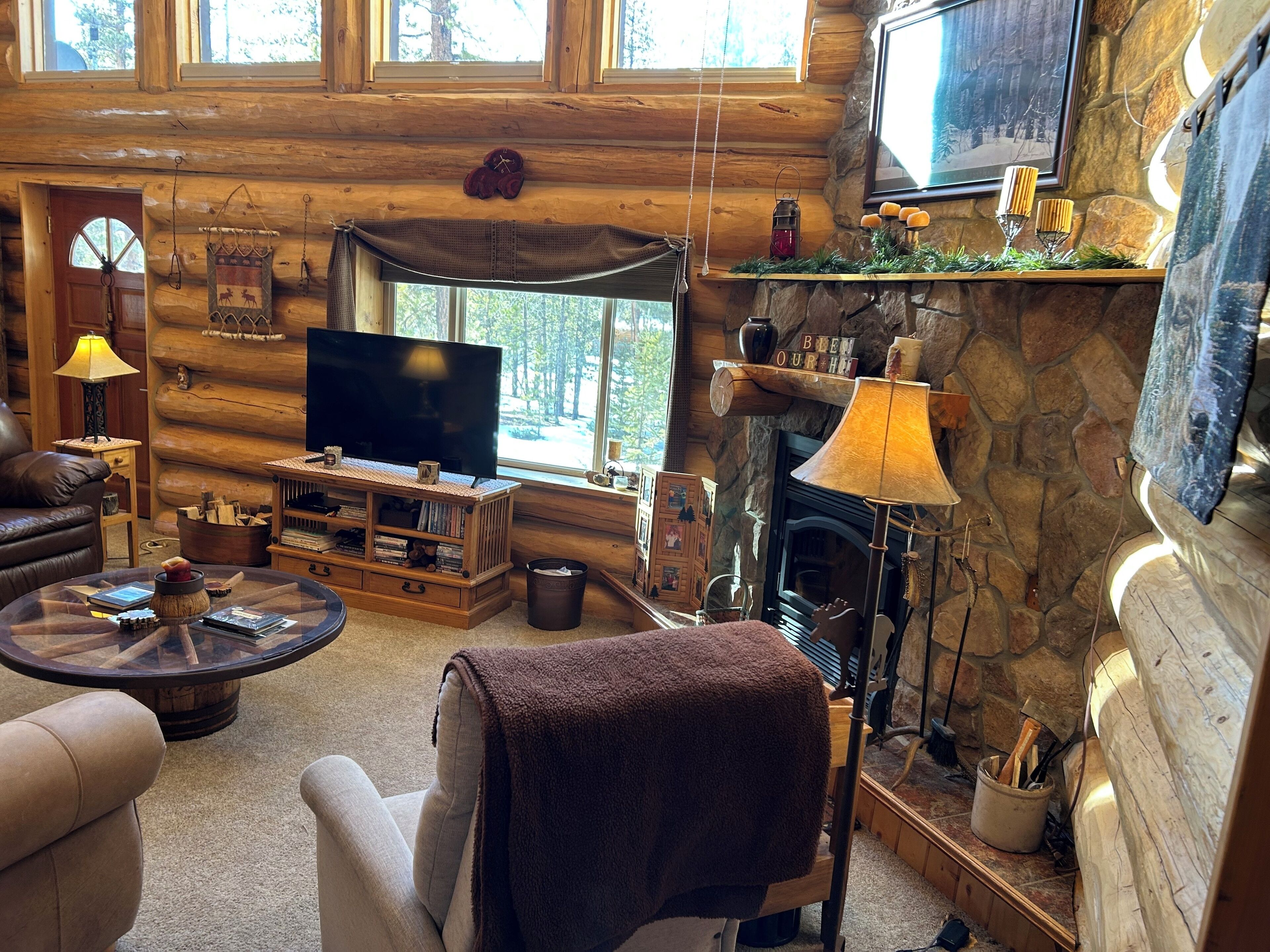 L’intérieur d’un chalet confortable, avec une cheminée, un téléviseur, un coin salon confortable et un mur en pierre.