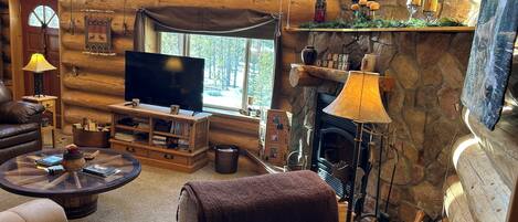 L’intérieur d’un chalet confortable, avec une cheminée, un téléviseur, un coin salon confortable et un mur en pierre.