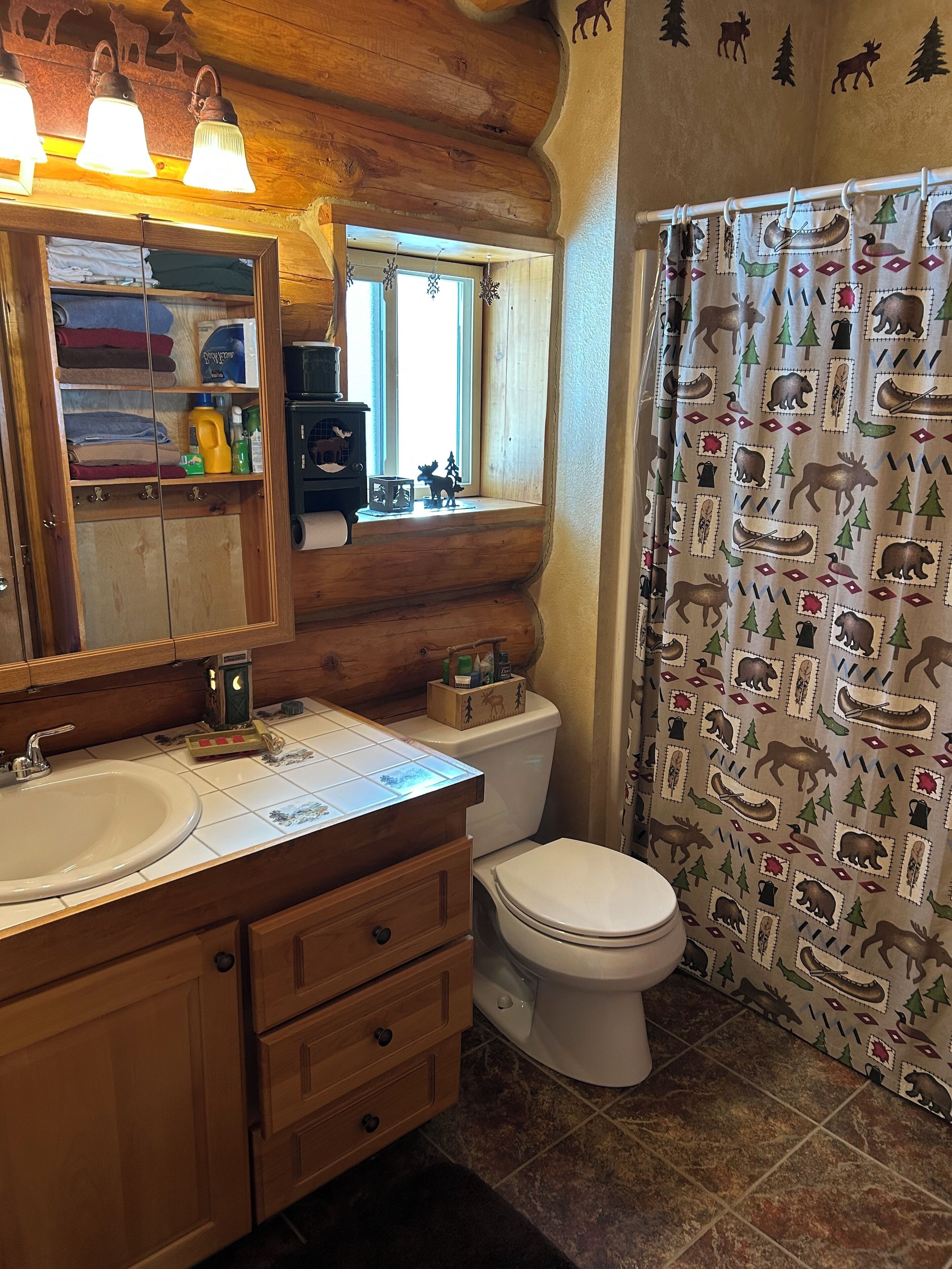 A rustic bathroom with wooden cabinetry, a sink, a toilet, and a shower curtain with a nature-themed pattern.
