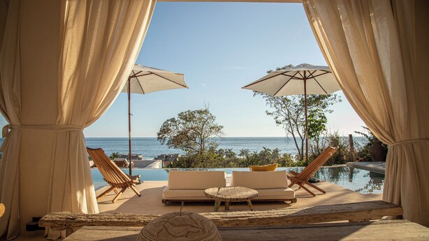 A poolside lounge area with a view of the ocean, featuring lounge chairs, umbrellas, and a wooden table. - Casa Selva, Troncones (Troncones)