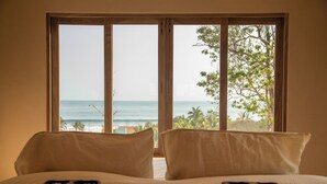 A bedroom with a large window offering a view of the ocean and palm trees. - Casa Selva, Troncones (Troncones)