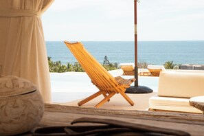A beachside lounge area with a wooden lounge chair, a white sofa, and a view of the ocean. - Casa Selva, Troncones (Troncones)