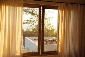 A window with wooden frames and beige curtains, offering a view of a rooftop with outdoor furniture. - Casa Selva, Troncones (Troncones)