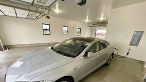 A white car parked indoors with a charging station, windows, and a ceiling with lights and ventilation. - 4 bedrooms & attached bathrooms, EV charge, water purifier, gas fireplace, games (Rexburg)