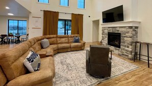 A spacious living room with a sectional sofa, a fireplace, and a large TV mounted on the wall. - 4 bedrooms & attached bathrooms, EV charge, water purifier, gas fireplace, games (Rexburg)
