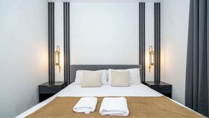 Une chambre d’hôtel avec un grand lit, deux tables de chevet et des lampes fixées au mur.