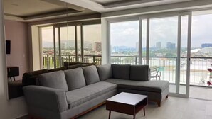 A modern living room with a grey sectional sofa, a small white coffee table, and large floor-to-ceiling windows offering a city view. - 508 New apartment, in Real Real View area 2 bedrooms (Zapopan)
