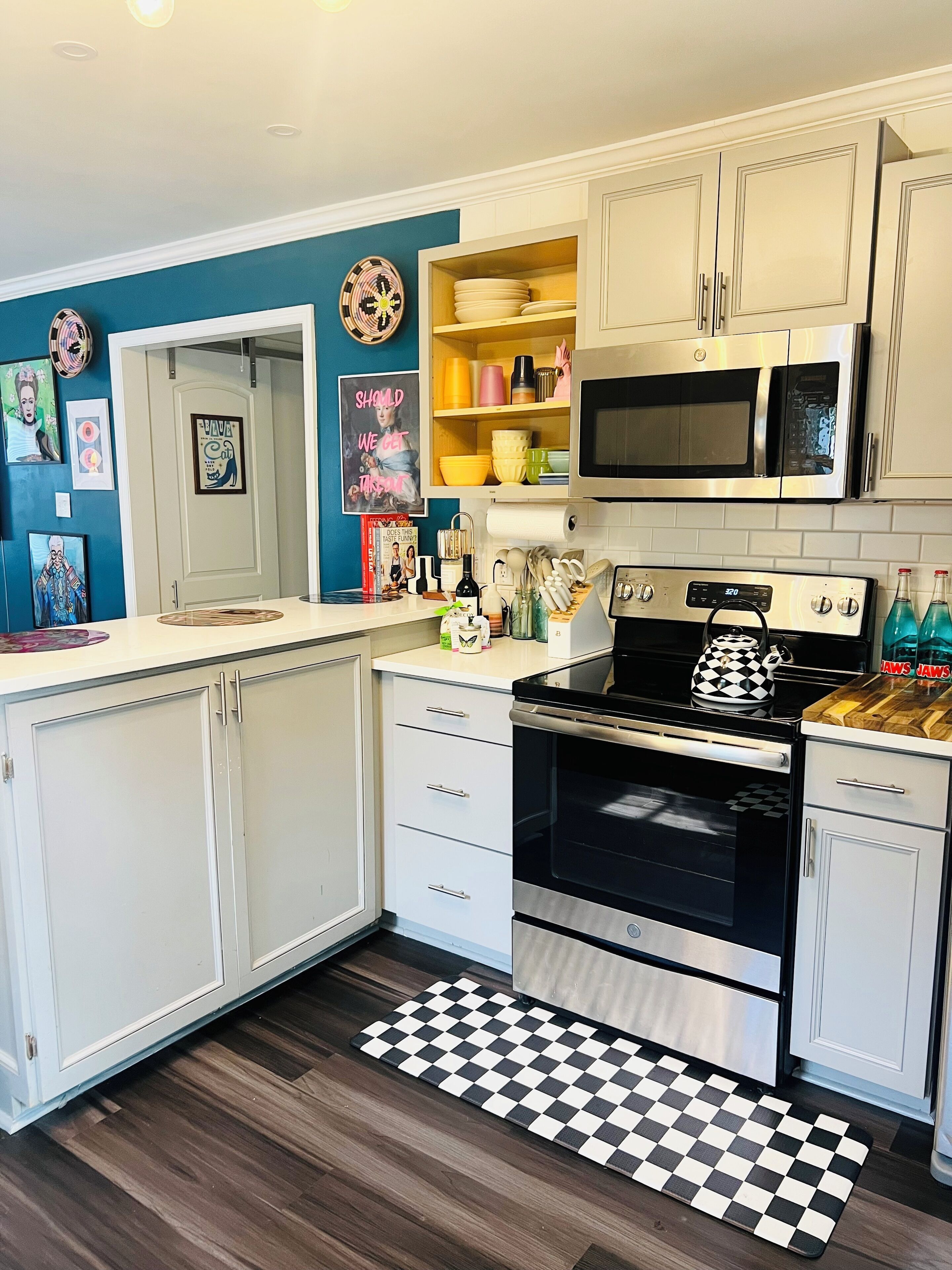 A modern kitchen with white cabinets, a stainless steel oven, a microwave, and a checkered floor mat.