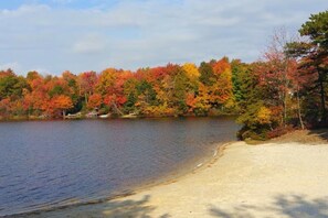 A lakeside view with autumn foliage, a sandy beach, and a dock. - Pocono Lakefront Villa-kayaks, firepl, skiing, gameroom+ (Long Pond)