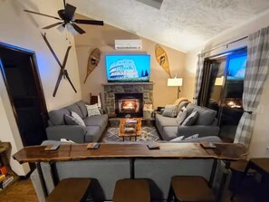 A living room with a fireplace, two sofas, a coffee table, and a TV. - Pocono Lakefront Villa-kayaks, firepl, skiing, gameroom+ (Long Pond)