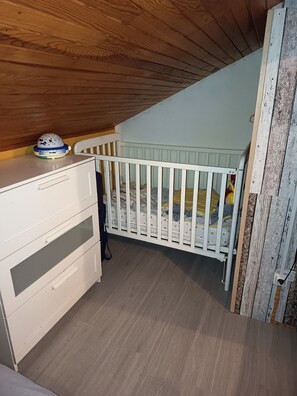 Una habitación con una cuna, un aparador y techo de madera.