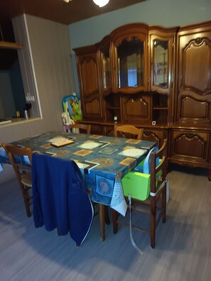 Un comedor con una mesa cubierta por un mantel estampado, rodeado de sillas de madera y un aparador de madera con un espejo.
