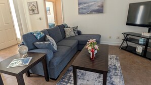 Ein Wohnzimmer mit einem Ecksofa, einem Couchtisch, einer TV-Konsole und einem Teppich.