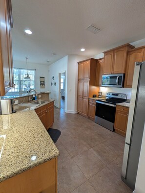 A kitchen with granite countertops, wooden cabinets, stainless steel appliances, and a window with blinds. - Tropical Oasis, Heated Pool, 7 mi to Beach , Dining , Golf (Englewood)