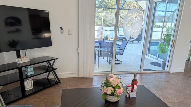 Ein Wohnzimmer mit Fernseher, einem Couchtisch mit Blumen und einer Flasche, und einer Glastür zu einer Außenpatio.