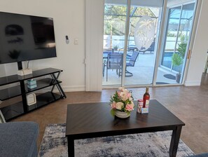 A living room with a TV, a coffee table with a flower arrangement and a bottle, and a sliding glass door leading to an outdoor patio. - Tropical Oasis, Heated Pool, 7 mi to Beach , Dining , Golf (Englewood)