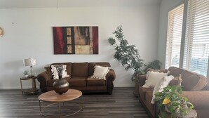 Un salon moderne avec un canapé marron, une table basse ronde et une grande fenêtre équipée de stores.