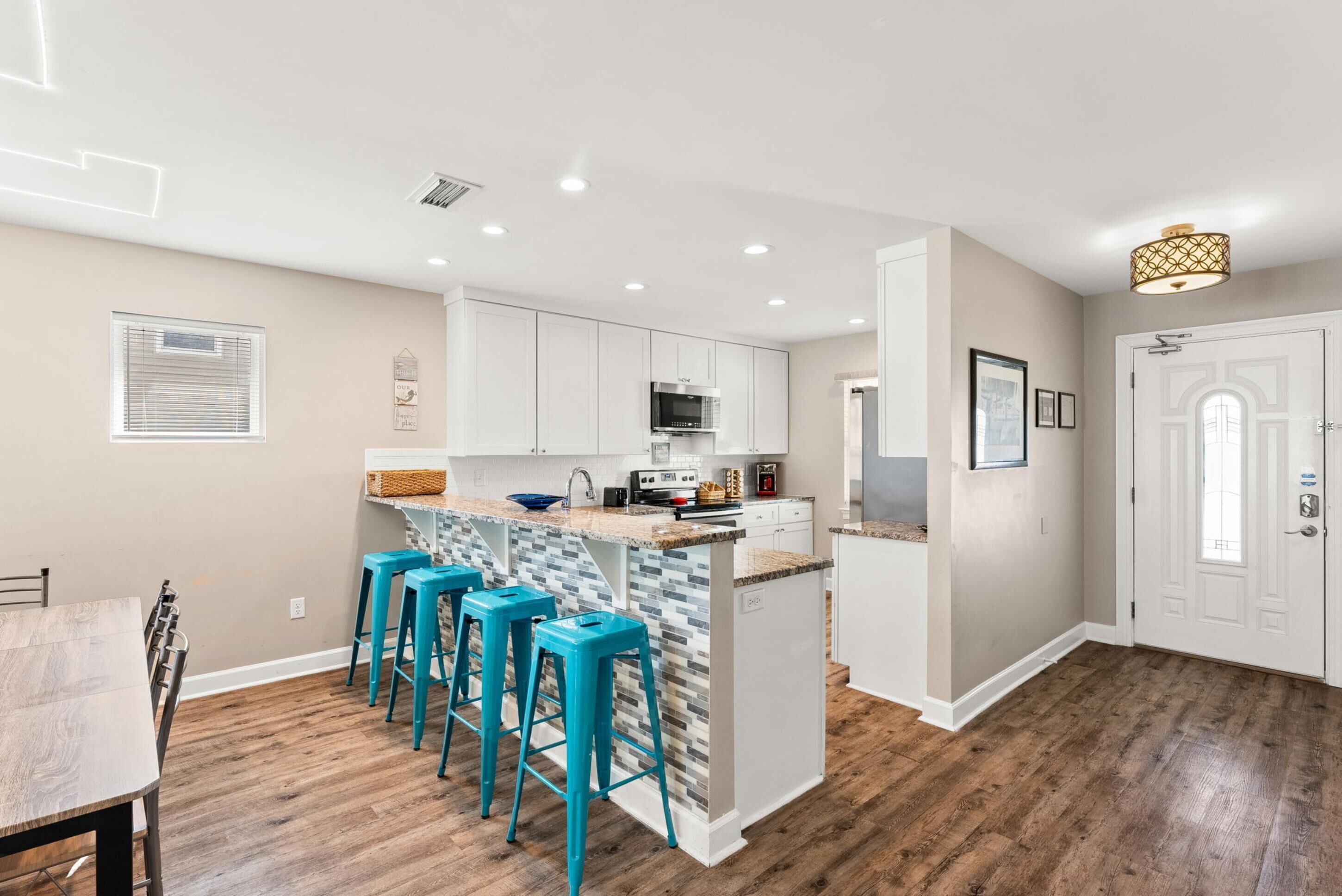 A modern kitchen with white cabinets, a central island with stools, and a dining area with a wooden table and chairs.