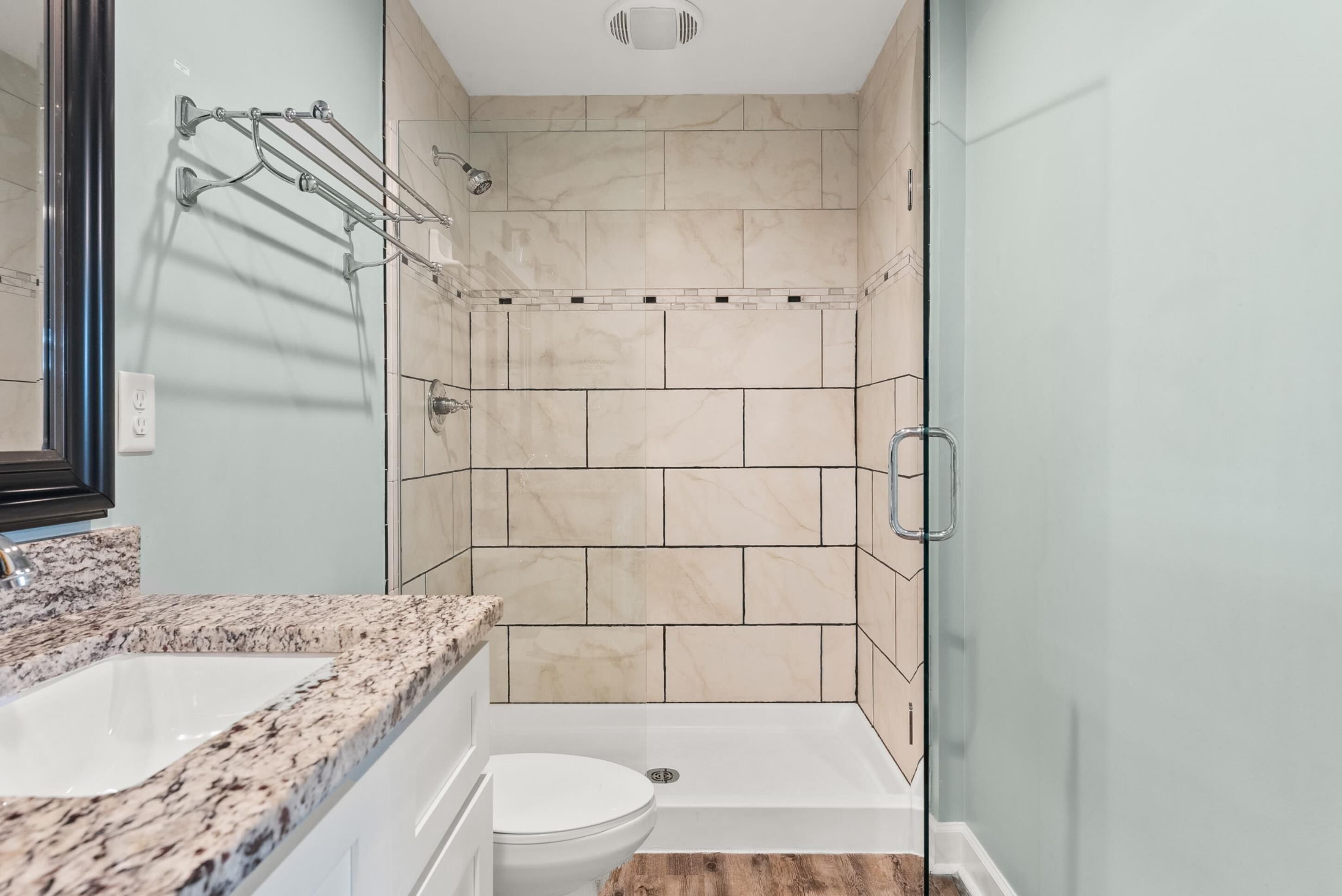 A bathroom with a marble countertop, a white toilet, and a glass-enclosed shower area with beige tiles.