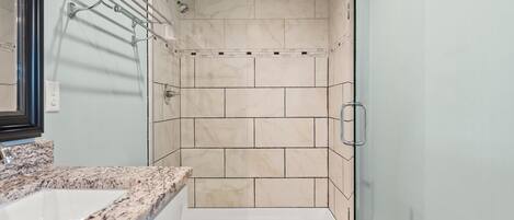 A bathroom with a marble countertop, a white toilet, and a glass-enclosed shower area with beige tiles.
