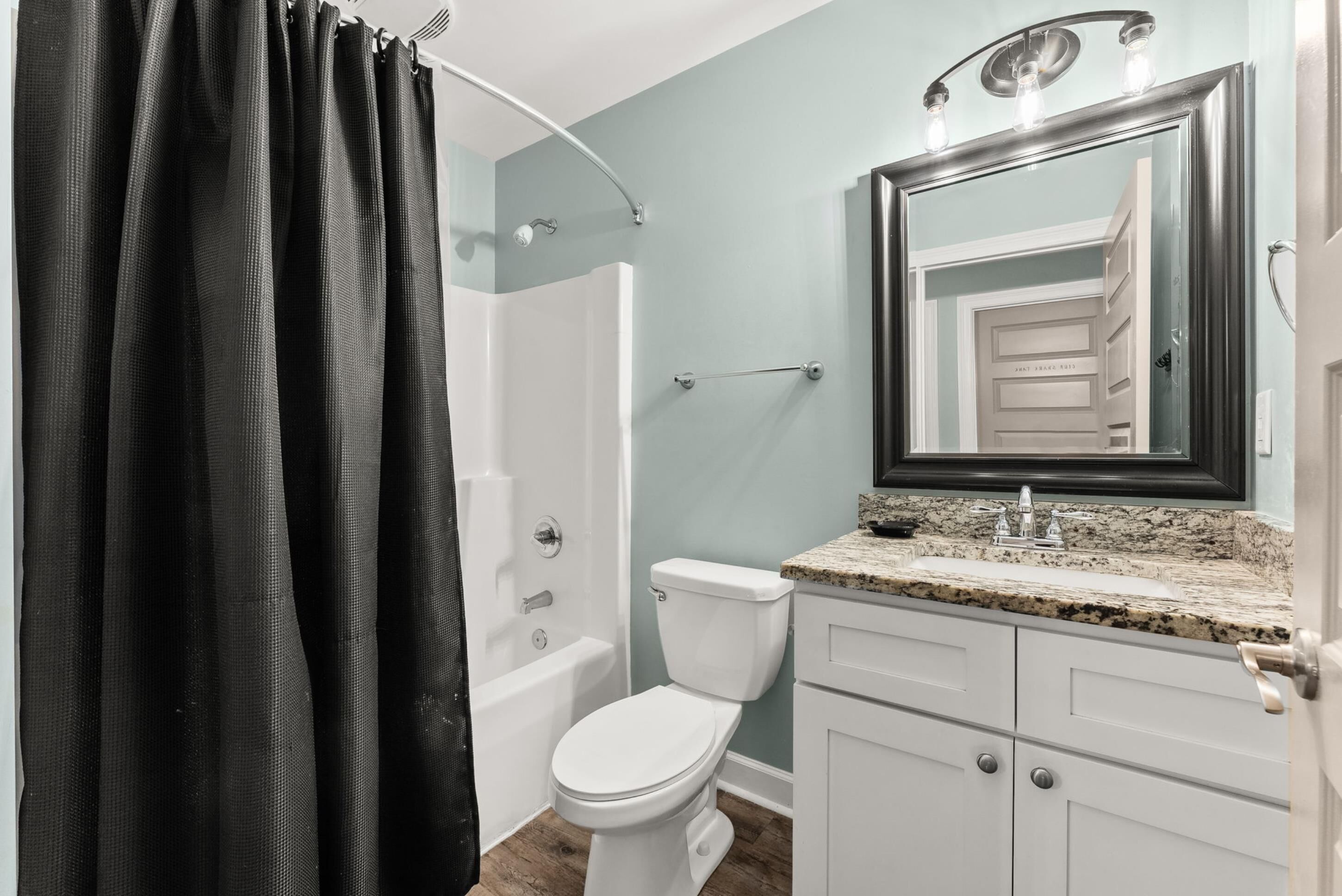 A bathroom with a shower, toilet, sink, and mirror.