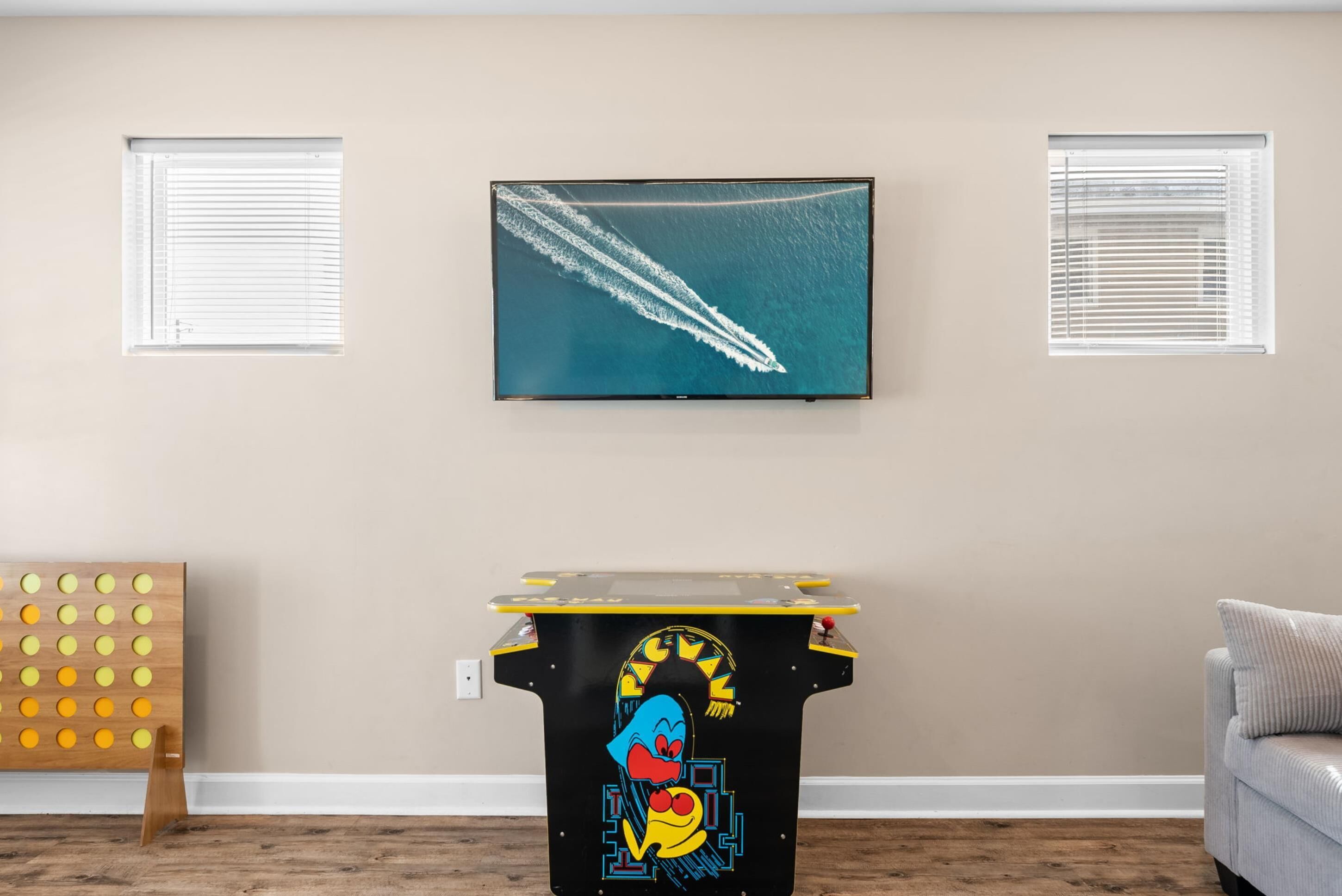A room with a large TV displaying a ship's wake, a Pac-Man arcade machine, and a couch.