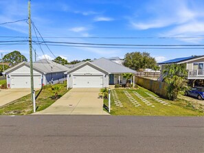 A residential area with two single-story houses, each with a garage, a small front yard with a palm tree, and a paved driveway. - Beach House - Sunset by the Sea (Panama City Beach)