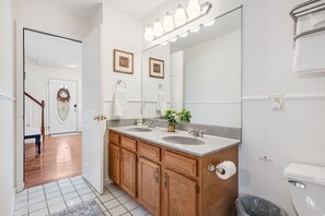 Une salle de bain avec des meubles en bois, un lavabo double, un grand miroir et un luminaire placé au-dessus du miroir.