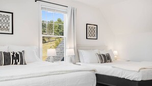 Ein Hotelzimmer mit zwei Betten, einem großen Fenster mit Blick auf Bäume und zwei gerahmten Bildern an den Wänden.