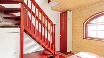 A room with a wooden staircase, a bed with a red bedspread, and a window with a view.