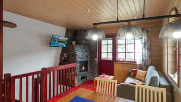 A cozy living room with a fireplace, wooden ceiling, and a red railing.