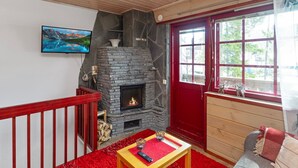 Ein gemütliches Wohnzimmer mit Kamin aus Stein, einer roten Tür und einem großen Fenster.