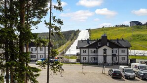 Ein Gebäude mit weißer Fassade und schwarzem Dach, gelegen auf einem Parkplatz mit mehreren Autos.