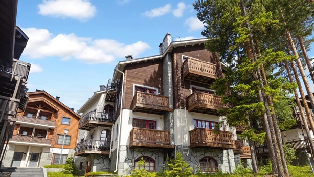 Ein mehrgeschossiges Gebäude mit hölzernen Balkonen, einer Fassade aus Stein und einem Weg zum Eingang.