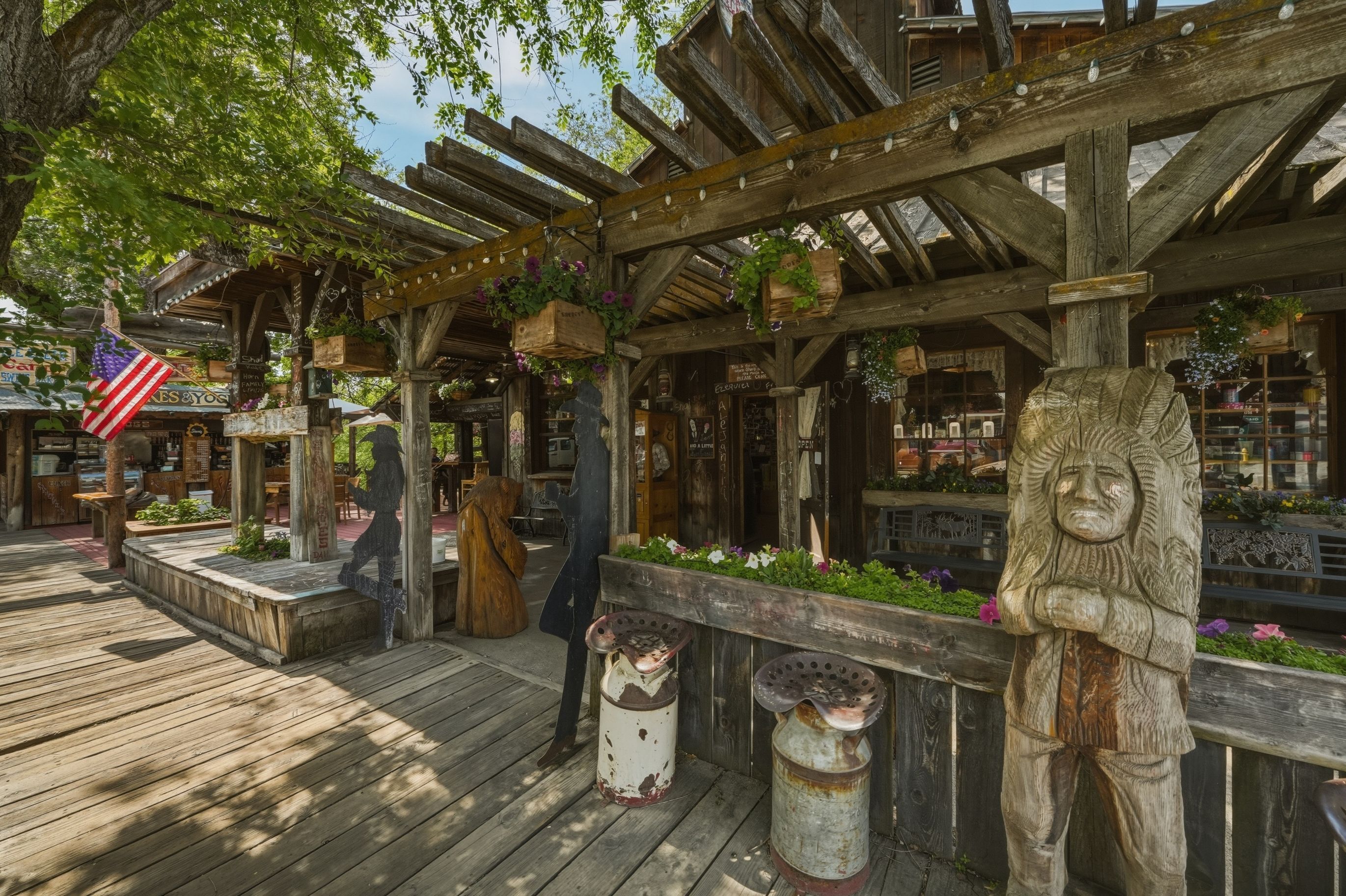 A rustic wooden structure with a covered porch, hanging flower baskets, and a statue.