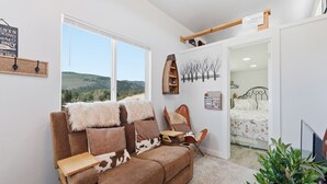 Un salon chaleureux avec un canapé marron, une étagère en bois et une vue sur l’extérieur.