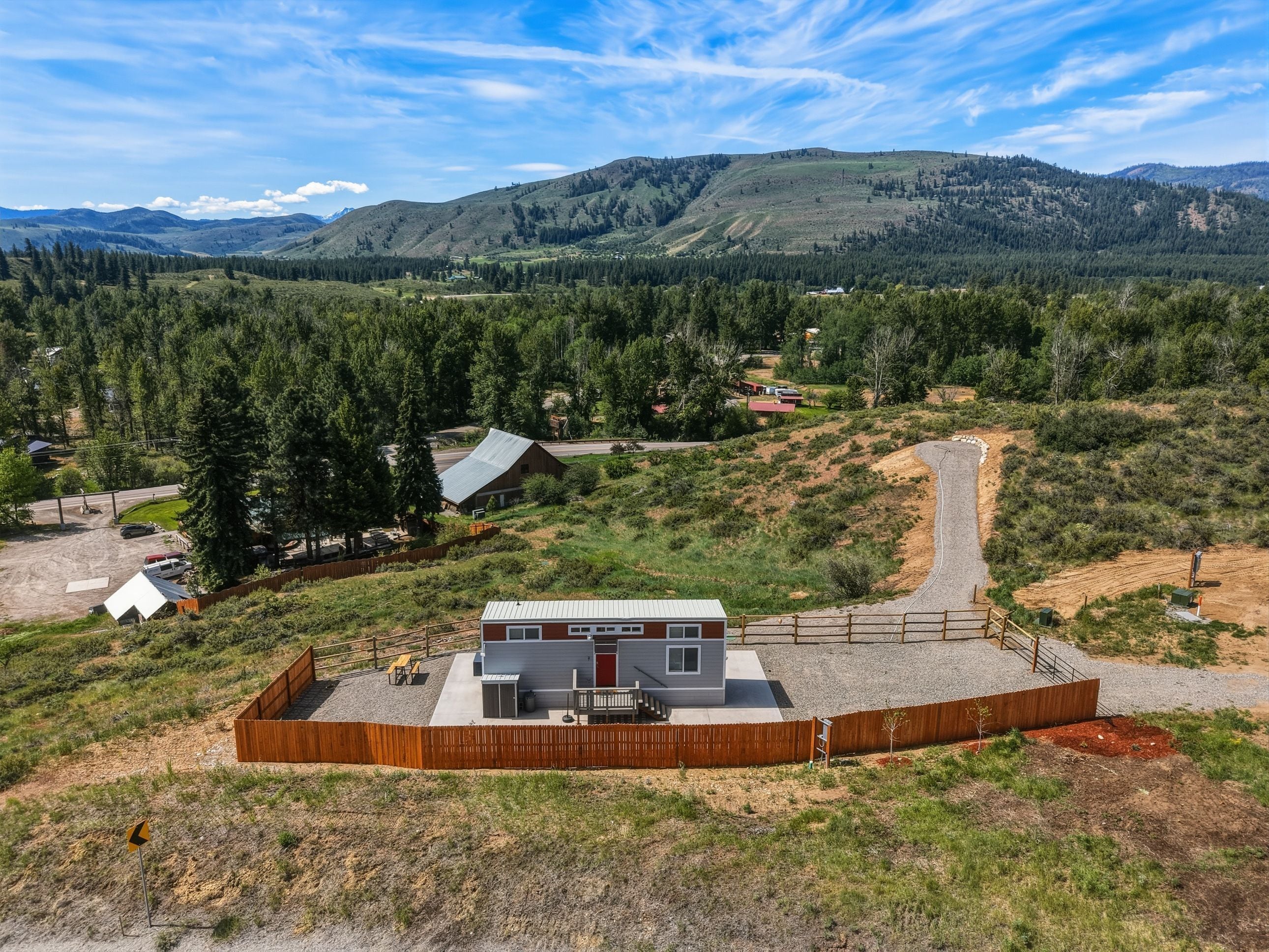 A modern building with a flat roof, surrounded by a wooden fence, set in a hilly landscape with a clear sky.